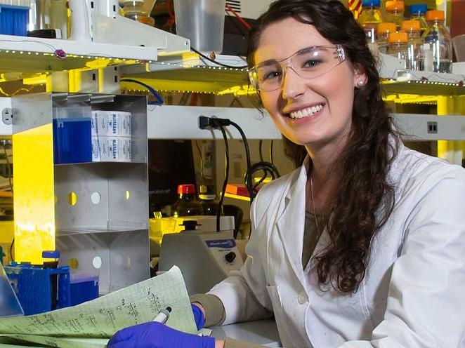 Woman wearing safety goggles and gloves taking notes smiling for a picture